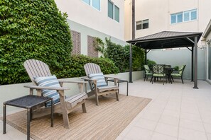 Eine Terrasse mit zwei Adirondack-Stühlen, einem kleinen Tisch und einem überdachten Sitzbereich.