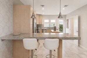 Une cuisine moderne dotée de plans de travail en granit, d’appareils électroménagers en acier inoxydable et d’un îlot central avec des tabourets de bar.