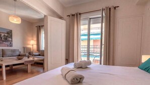 A hotel room with a bed, a sitting area with a table and chairs, and a balcony with a view. - Acropolis museum grand apartment (Athina)