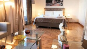 A hotel room with a bed, two bedside tables, a glass coffee table, a lamp, a painting on the wall, and a statue on the floor. - Stunning Acropolis view apartment (Athina)