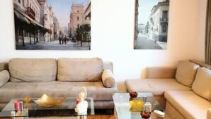 A modern living room with two sofas, a glass coffee table, and a herringbone wood floor. There are two framed pictures on the wall and a ceiling light fixture. - Stunning Acropolis view apartment (Athina)