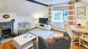 A cozy living room with a fireplace, a television, a dining table with chairs, and a window with curtains. - Host & Stay | Park Place Apartment (Whitby)