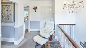 A hallway with a white chair, a wooden bench, a chandelier, and a door. - Host & Stay | Park Place Apartment (Whitby)