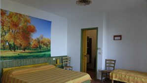 Une chambre avec deux lits, un tableau représentant des arbres d’automne, une chaise en bois et une porte donnant sur une autre pièce.