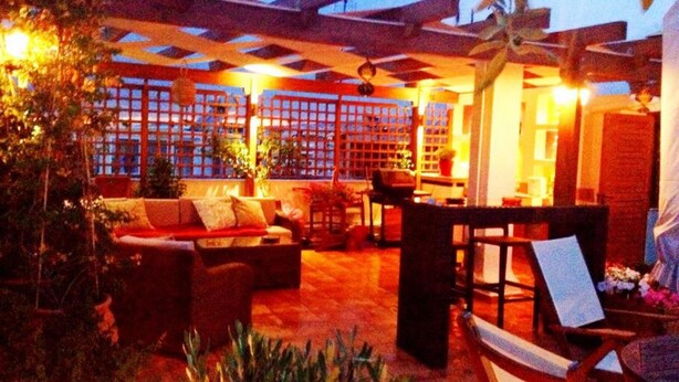 Un'area patio esterna con un pergolato in legno, un divano e un tavolo da pranzo.