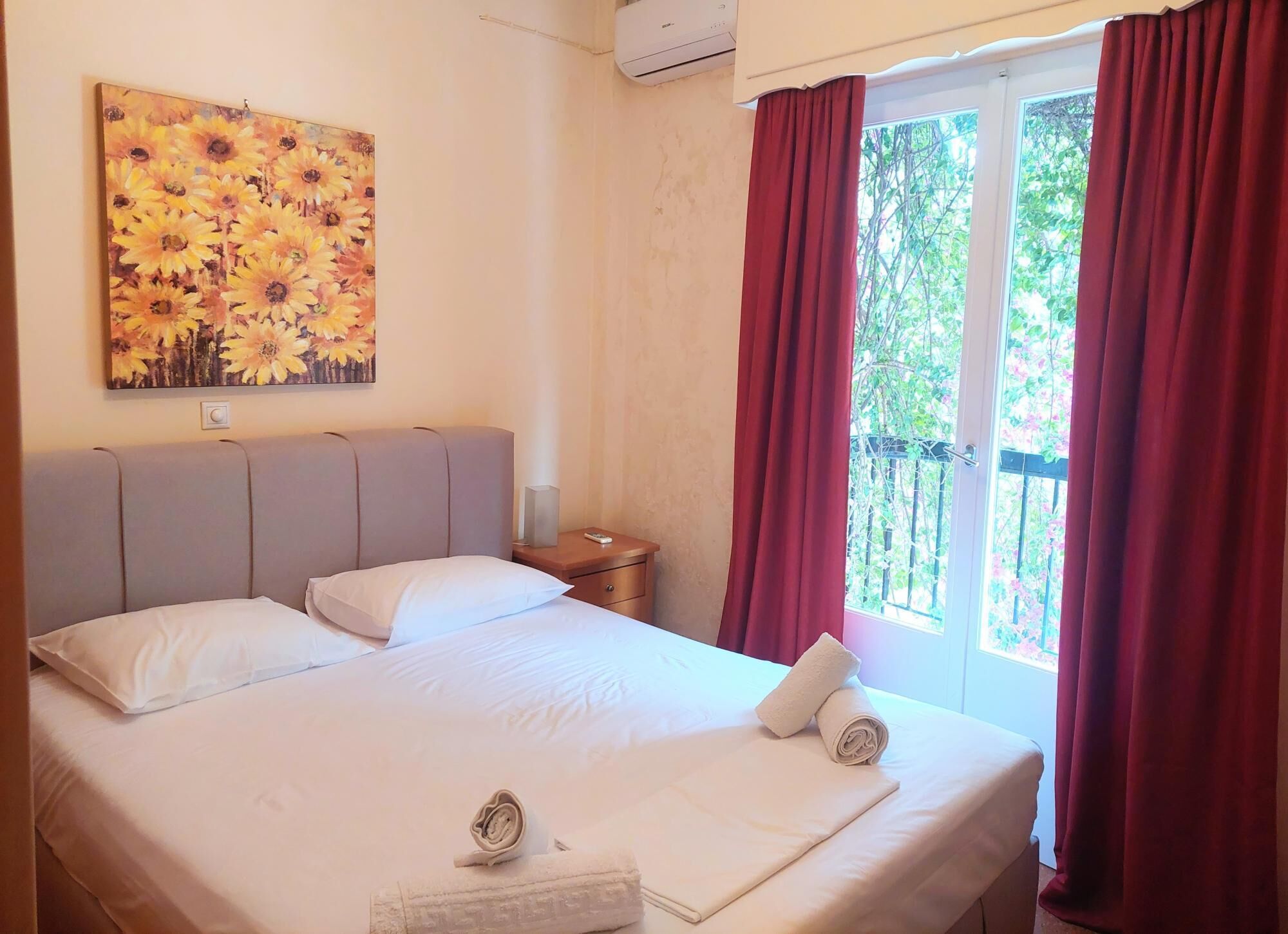 Una habitación de hotel con una cama, una mesita de noche, un cuadro de girasoles y cortinas rojas.