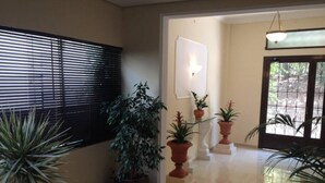 Un corridoio con piante in vaso, un lampadario e una porta che dà sull'esterno.