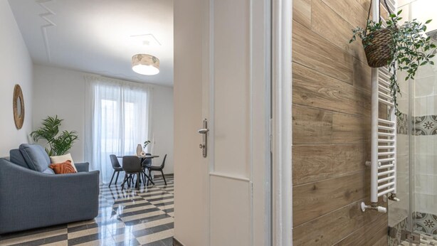 A modern living room with a sofa, dining table, and chairs, a hallway with a checkered floor, and a wooden wall with a radiator.