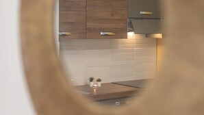 A view through a circular mirror reflecting a kitchen with wooden cabinets, a tiled backsplash, and a countertop with a small plant.