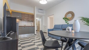A modern kitchen with grey cabinets, a black countertop, and a checkered floor. There is a blue sofa and a round table with a vase and candle.
