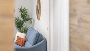 A cozy living room with a blue sofa, a potted plant, and a decorative mirror on the wall.