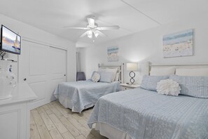 A bedroom with two beds, a ceiling fan, a TV, and artwork on the walls. - Beach-side, beautiful low-rise with uncrowded beach! (Destin)