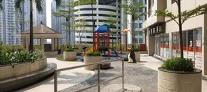 A playground with slides and a climbing structure, surrounded by planters and a gazebo.