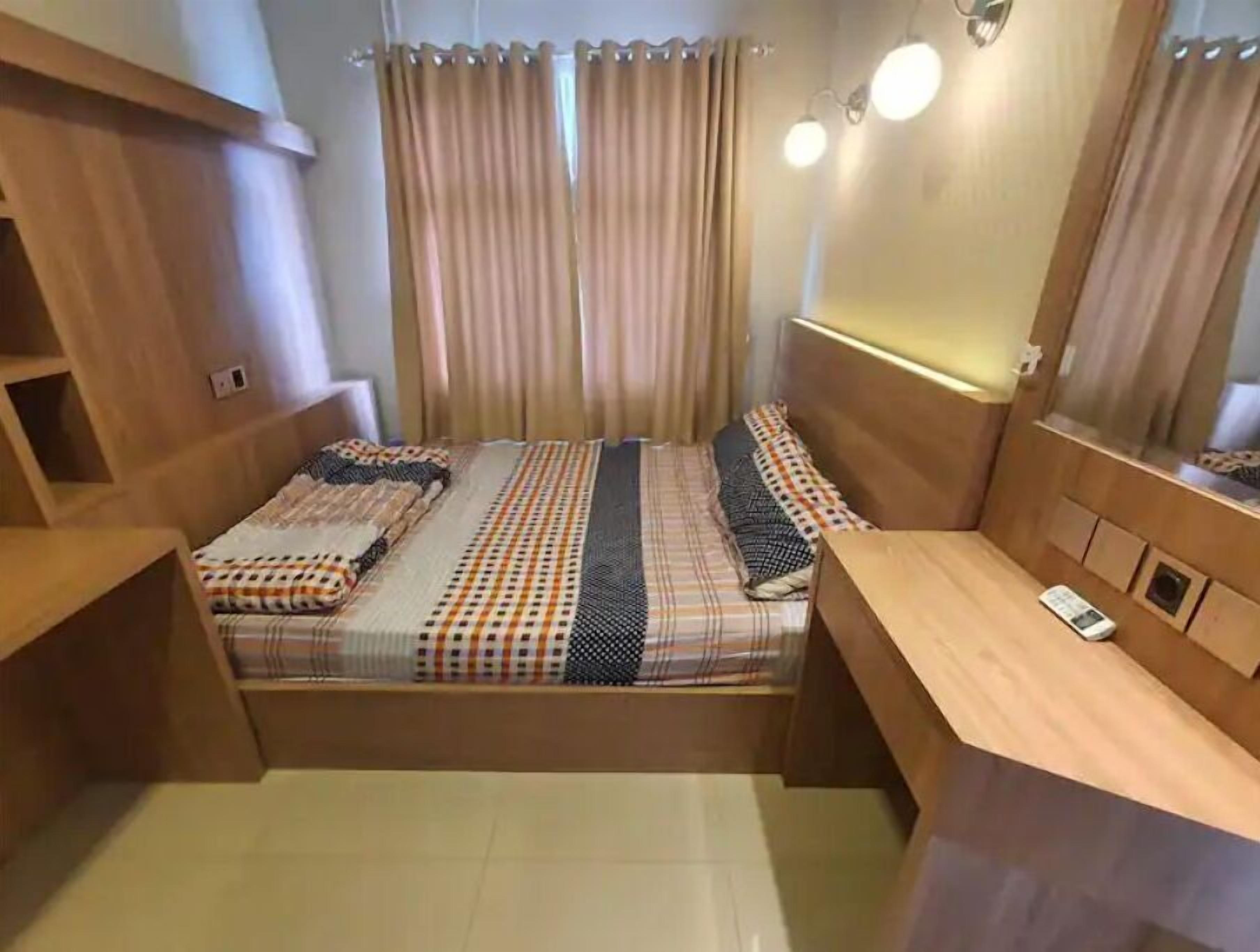 Une chambre à coucher de taille modeste, comprenant un lit, des tables de chevet, un miroir et des rideaux.