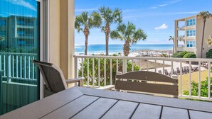 A balcony with a view of the beach, palm trees, and a building across the water.