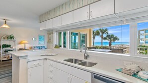 A modern kitchen with white cabinetry, a stainless steel sink, and a view of the ocean.