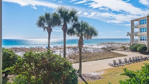 A beach view with palm trees, a pool area with lounge chairs, and a building with balconies overlooking the ocean.