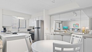 A modern kitchen with white cabinetry, a stainless steel refrigerator, and a dining area with a round table and chairs. - Freshly renovated! Beachfront property! (Destin)