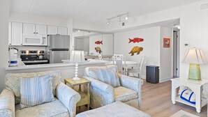 A modern living room with patterned sofas, a dining area, and a kitchen with white cabinets and appliances. - Freshly renovated! Beachfront property! (Destin)