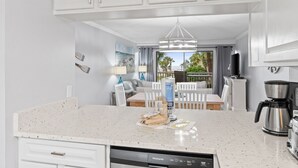 A modern kitchen with white cabinetry, a built-in dishwasher, a coffee maker, and a view of the outdoors.