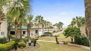 A resort courtyard with palm trees, a swimming pool, and a building with a green roof.