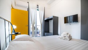 Ein Hotelzimmer mit einem Bett, einem an der Wand montierten Fernseher, einem Kleiderschrank und einem Fenster mit Vorhängen.