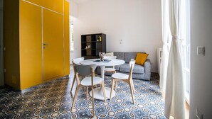 Ein Zimmer mit einem runden Tisch, vier Stühlen, einem grauen Sofa mit gelbem Kissen, einem Bücherregal und einem gelben Kleiderschrank.