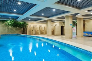 Una piscina interior con agua cristalina, rodeada de paredes y columnas color beige, y un techo con diseño de cuadrícula.