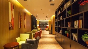 A hotel lobby with a long, narrow layout featuring a row of armchairs and a bookshelf filled with books and plants. - Xixia Kunpeng Hotel (Xixia)