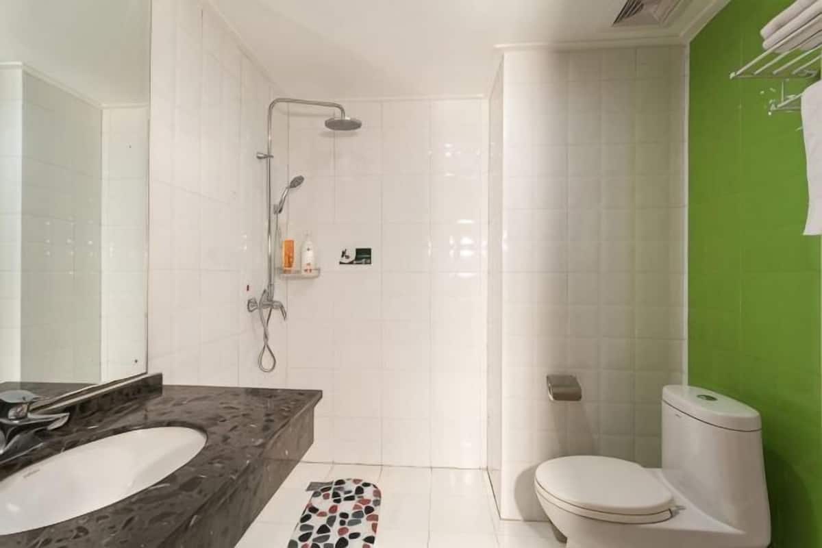 A bathroom with a white sink, a toilet, a shower, and a green accent wall.