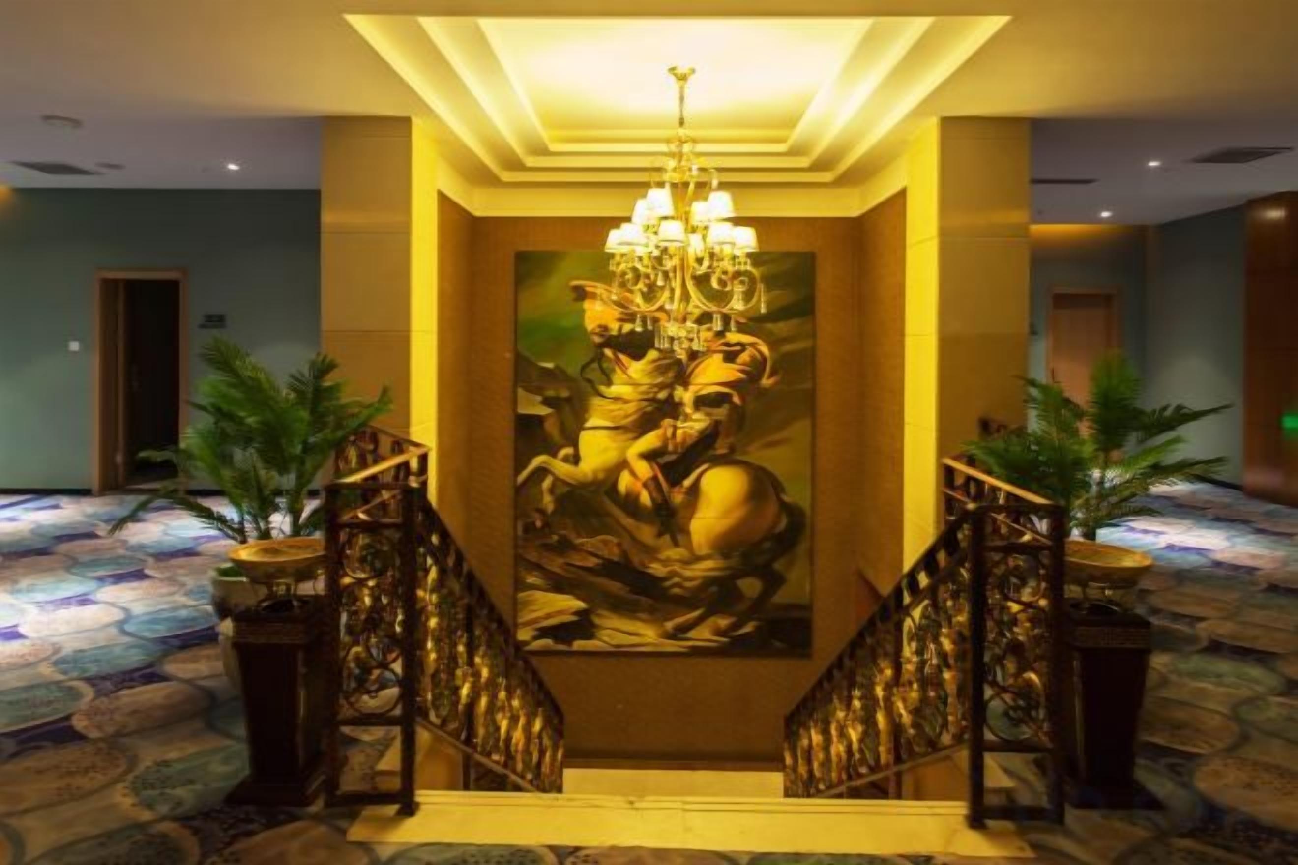 A grand staircase with a chandelier, flanked by potted plants, leading to a room with a large mural.