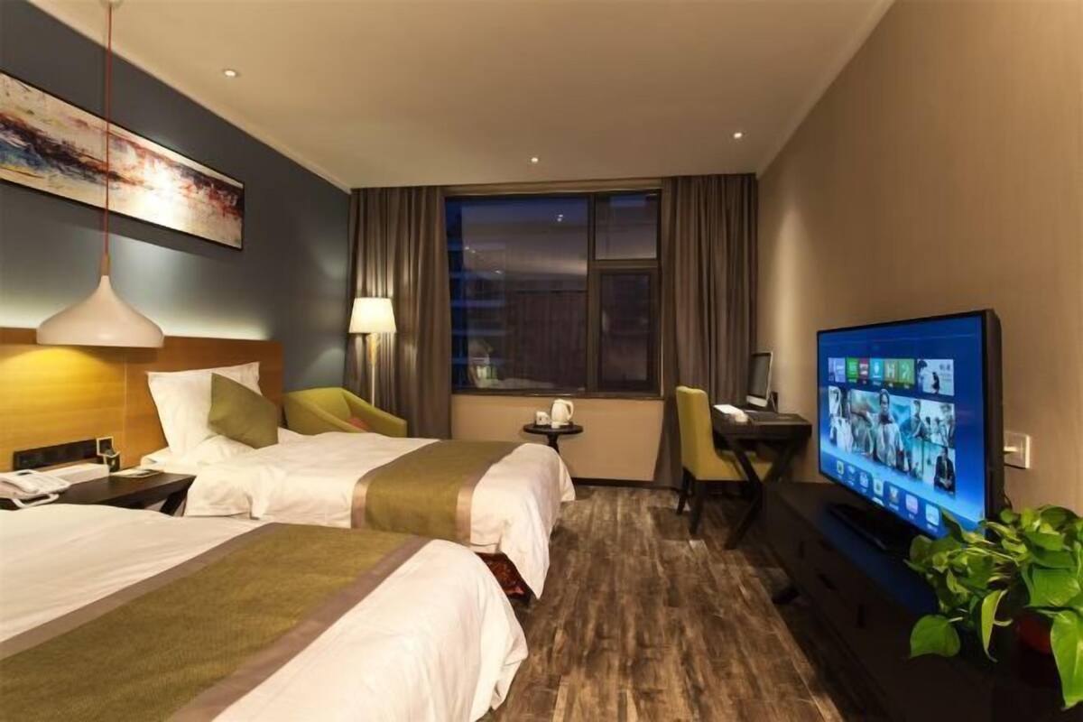 A hotel room with two beds, a desk, a television, and a window.