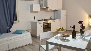 A compact living space with a kitchenette, a dining area, and a bed with blue pillows. - Salento Casa Relax (Vignacastrisi)