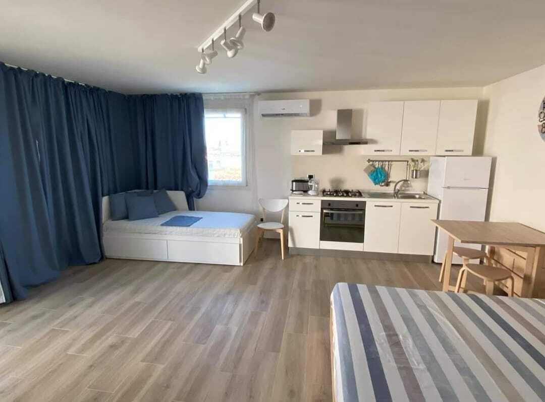 A compact room with a bed, a small kitchenette, a dining table, and a window with curtains.