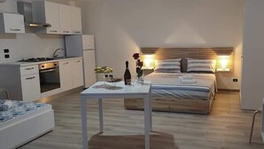 A modern bedroom with a bed, bedside table, and a small kitchen area with a stove and cabinets. - Salento Casa Relax (Vignacastrisi)