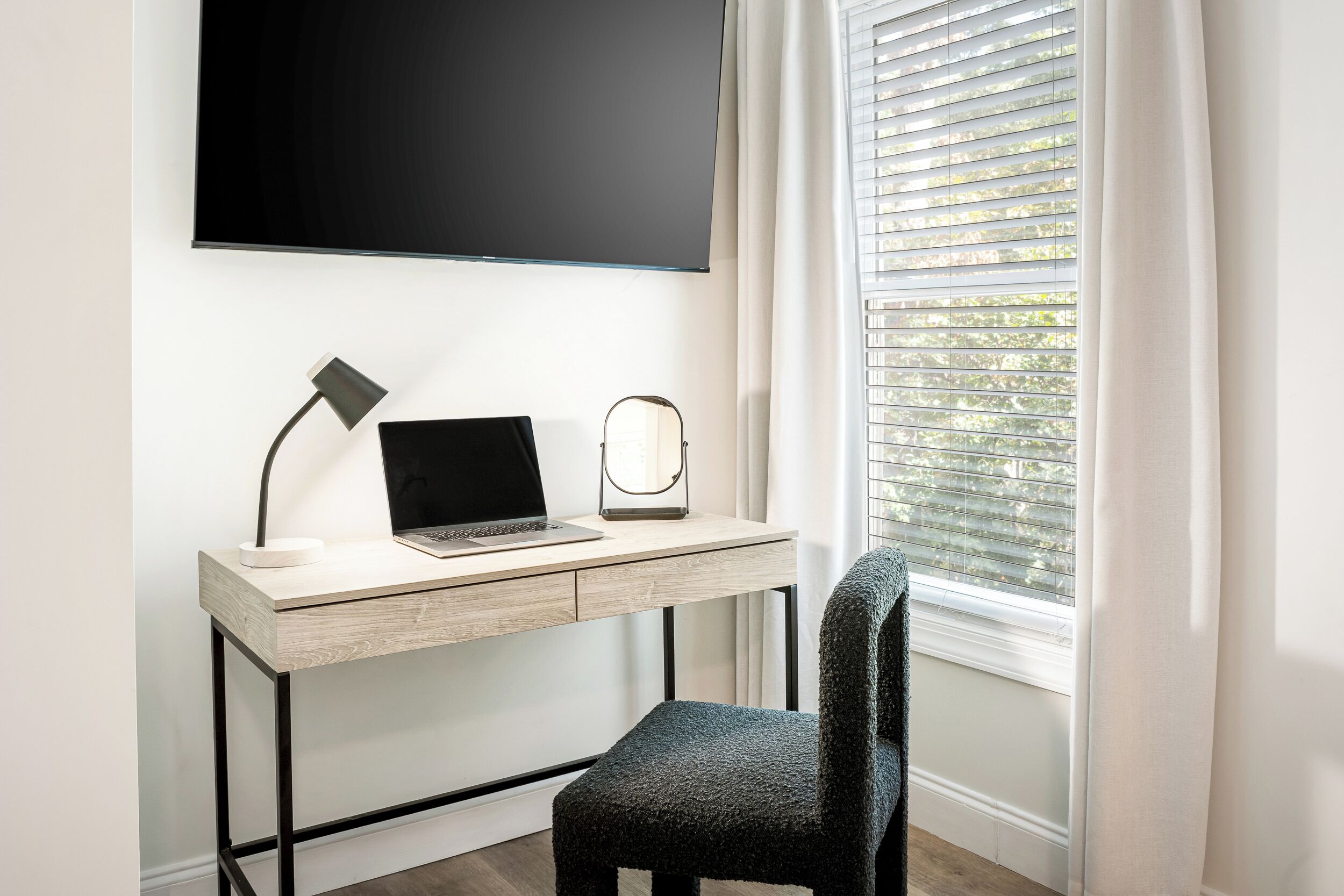 Un espacio de trabajo moderno con una computadora portátil sobre un escritorio de madera, una lámpara y una silla.