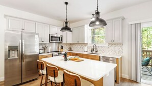 A modern kitchen with white cabinets, stainless steel appliances, a large island with bar stools, and pendant lighting. - Top Shenandoah Stay | 4BR w/ 2 King Suites | Private | Easy Drive | Newly Built (McGaheysville)
