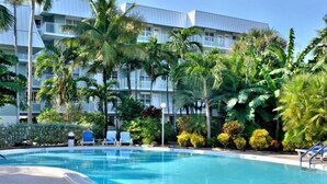 A swimming pool with lounge chairs, surrounded by palm trees and a multi-story building with balconies. - The Crown Jewel of La Brisa 2 bdrm Monthly Spectacular ocean views. (Key West)