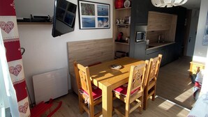 Un espace de vie compact comprenant une table et des chaises en bois, un petit coin cuisine avec un micro-ondes et un évier, et un téléviseur fixé au mur.