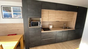 Une cuisine de taille réduite, dotée de meubles de rangement sombres, d’un four à micro-ondes, d’un évier et d’un plan de travail en bois.