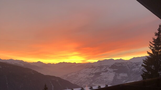 Un balcon offrant une vue sur des montagnes enneigées et un coucher de soleil.