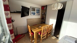 Un coin repas avec une table et des chaises en bois, un téléviseur fixé au mur et un luminaire suspendu au plafond.