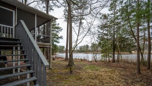 A cabin with a wooden staircase leading to a covered porch overlooking a lake surrounded by trees. - Close to Lewes with community pool, tennis & a fishing pier! 23290 Bridgeway (Lewes)