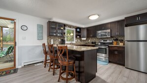 A modern kitchen with dark wooden cabinets, a stainless steel refrigerator, and a granite countertop island with bar stools. - Close to Lewes with community pool, tennis & a fishing pier! 23290 Bridgeway (Lewes)