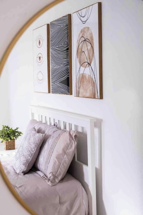 Een slaapkamer met een wit hoofdbord, een bed met twee kussens, en een kunstwerk aan de wand boven het bed.