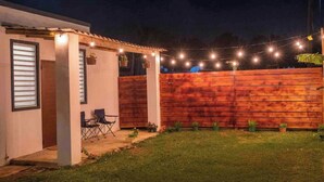 Ein Patio mit Holzzaun, Lichterketten und einer kleinen Sitzgruppe mit Stühlen.