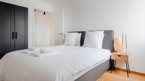 A modern bedroom with a large bed, a wardrobe, and a bedside table with a lamp.