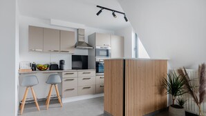 A modern kitchen with beige cabinets, a wooden island, two grey bar stools, and a potted plant.