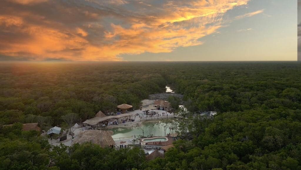 Un resort con piscina, estructuras de techo de paja y vistas a un río.