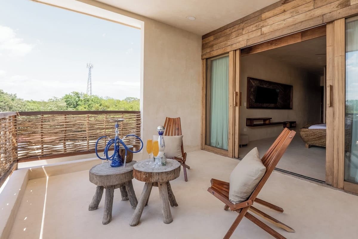 A balcony with a wooden table, chairs, a hookah, and a glass of orange juice.